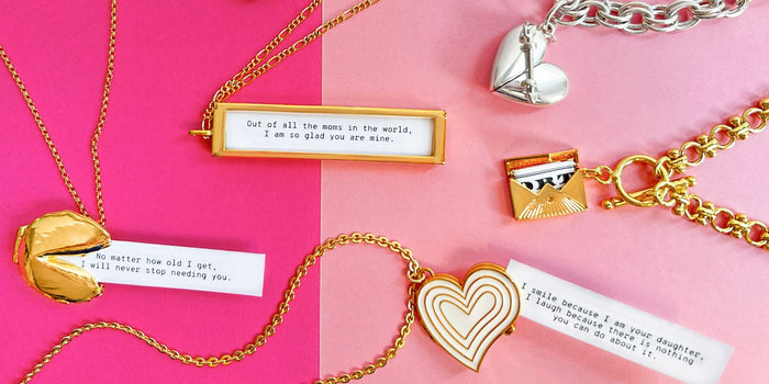 Gold Fortune Cookie Locket holding fortune, Gold Deco Heart Locket holding fortune (Ivory), Gold Love Letter Envelope Locket open showing fortune, Silver Heart + Arrow bracelet, and Gold Classic Fortune Locket holding fortune.